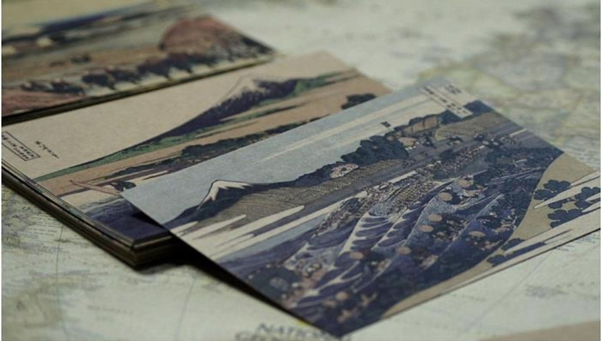 Hokusai Japanese Art Postcards: Ukiyo-e scenes in muted colors on paper, stacked on a map.